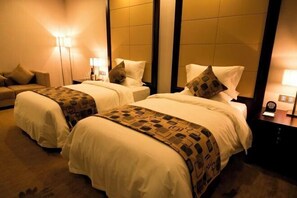 A hotel room with two beds, each with a patterned throw blanket and pillows. There is a nightstand with a lamp and a clock on the right side. - Sunwu Hot Spring International Hotel (Huimin)