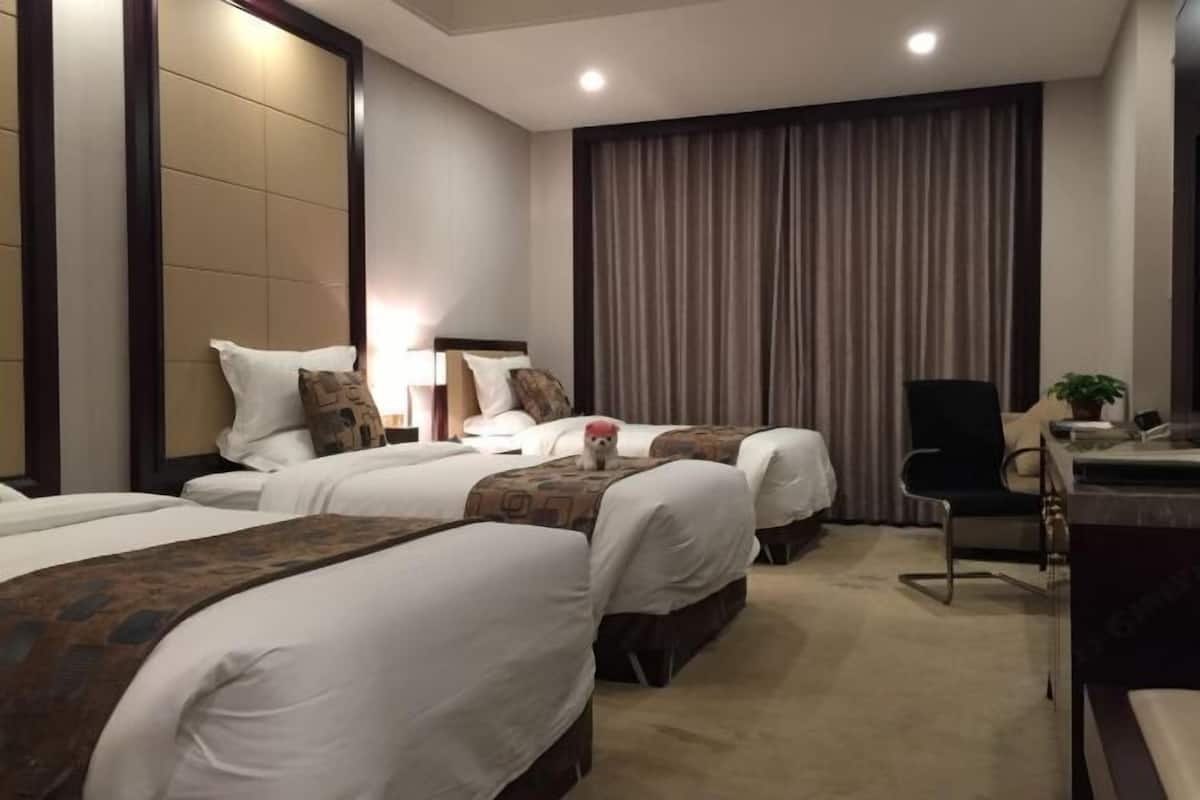 Habitación de hotel con dos camas, un escritorio, una silla y un ventanal con cortinas.