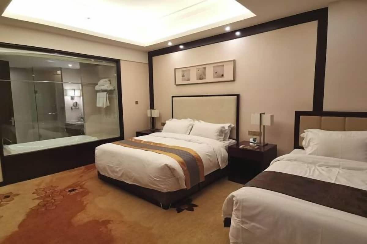 Habitación de hotel con una cama grande, una mesita de noche, una mampara de cristal para la ducha y suelo cubierto de alfombra.