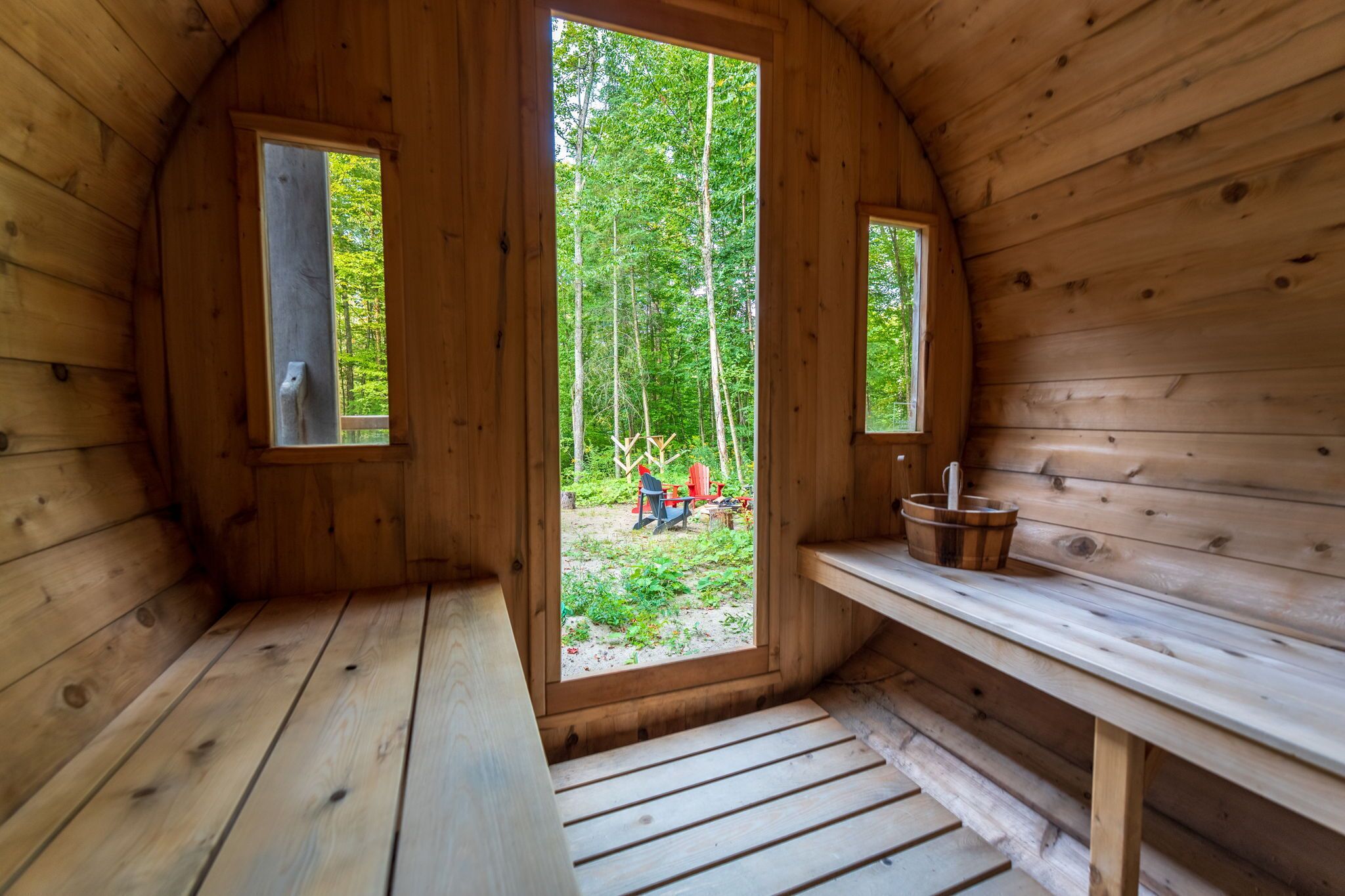 Eine Holzhütte mit einer Bank, einem Tisch und zwei Fenstern mit Blick auf den Wald.