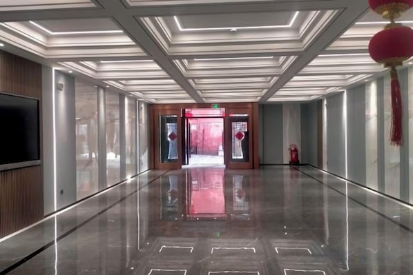 Un pasillo con piso reflectante, un televisor de pantalla plana a la izquierda y una puerta roja al final.