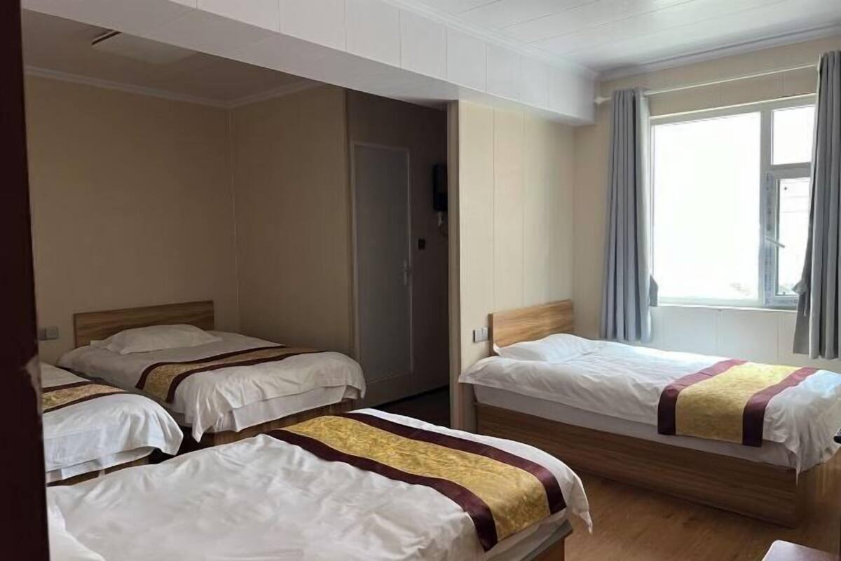 A hotel room with three single beds, a window with curtains, and a door leading to another room.