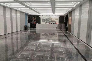 A modern hotel lobby with a marble floor, a reception desk, and a wall-mounted artwork.