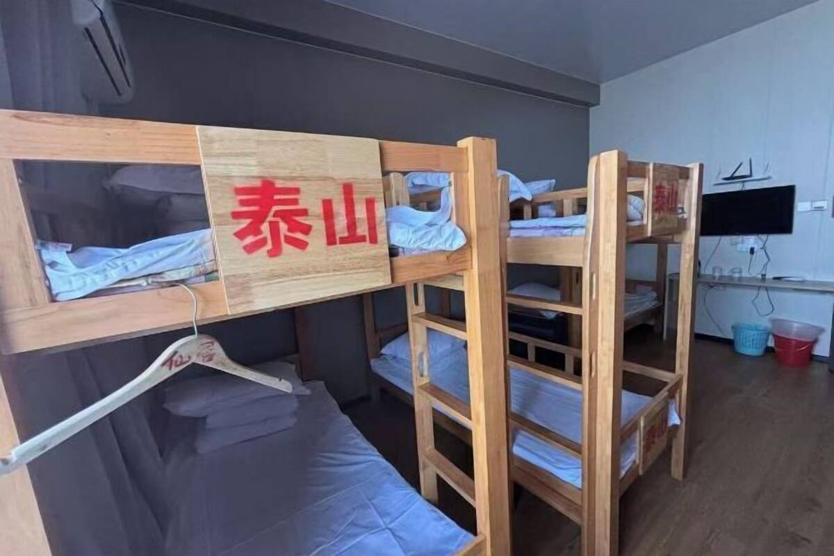 A bunk bed room with a wooden frame, a TV mounted on the wall, and a wooden sign with red text.