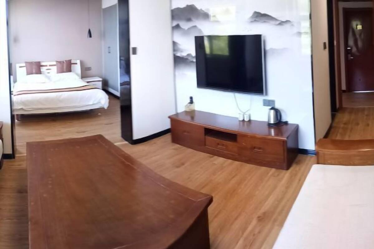 A hotel room with a bed, a wooden bench, a TV, and a wall-mounted cabinet.