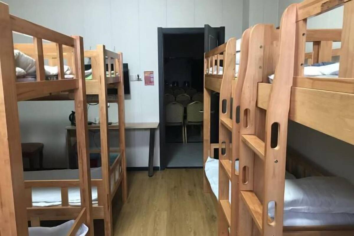 A dormitory room with bunk beds, a desk, and a chair.