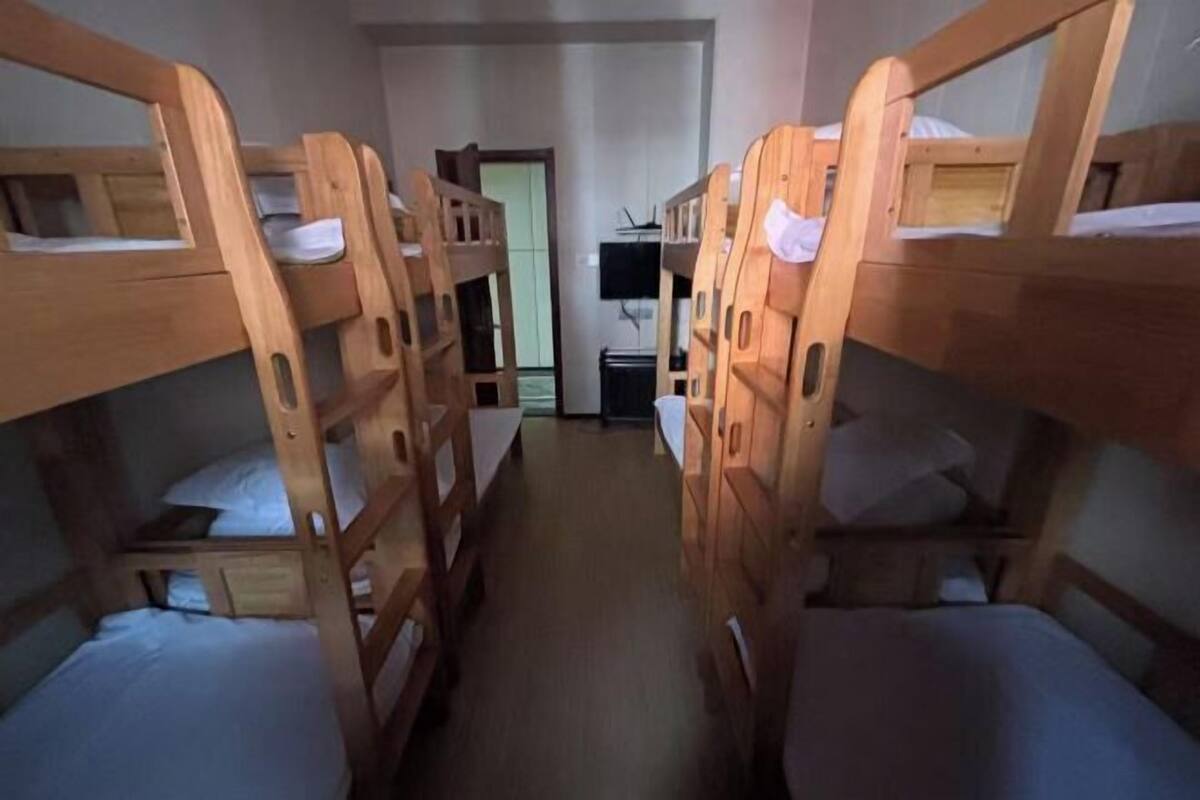 A room with bunk beds arranged in a row, a television mounted on the wall, and a door leading to another room.