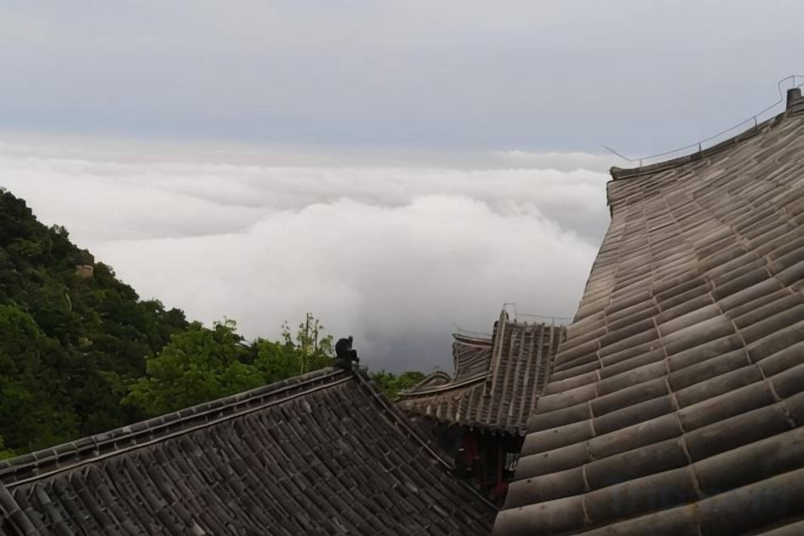 Arquitectura tradicional con techos empinados y una vista de un valle cubierto de nubes.