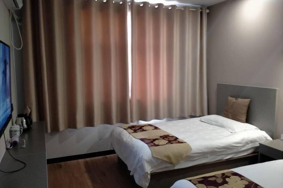 A hotel room with a bed, a nightstand, a TV, and curtains.