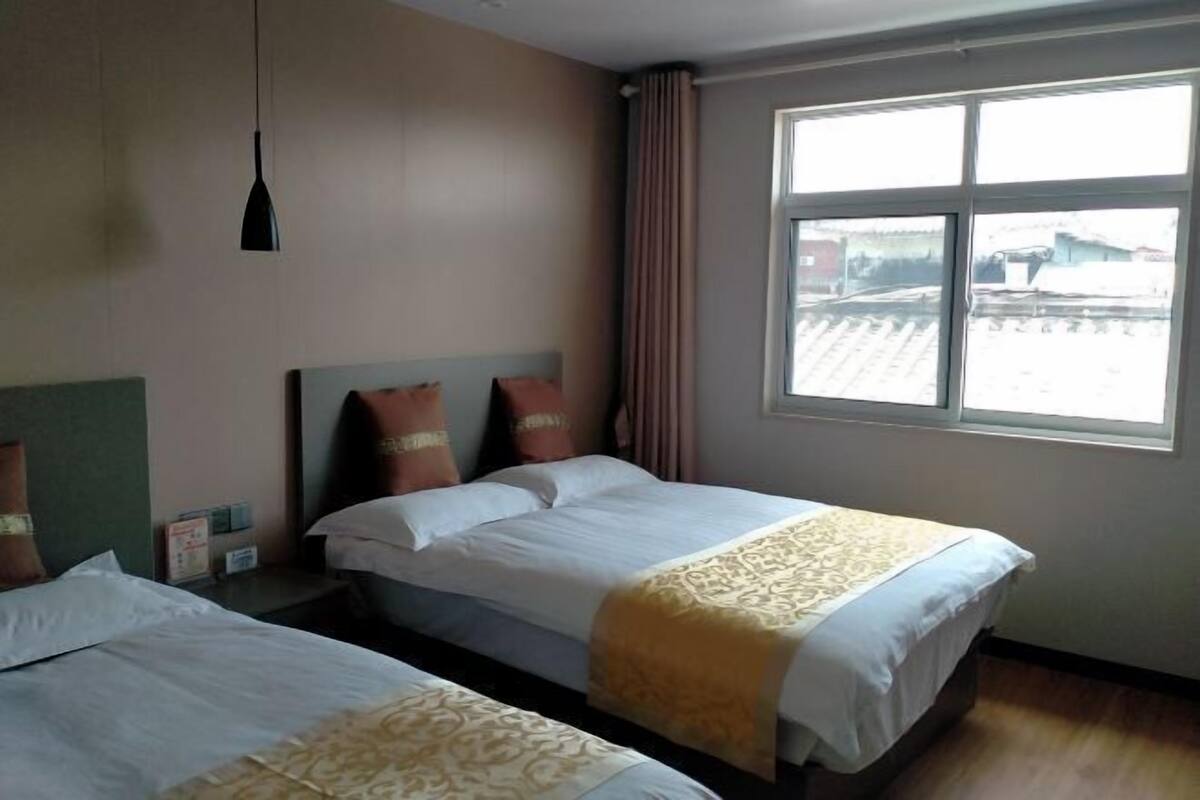 A hotel room with two beds, a window with a view, a hanging pendant light, and a curtain.