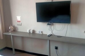 Una habitación con una televisión de pantalla plana montada en la pared, una mesita con una tetera, tazas y un control remoto.