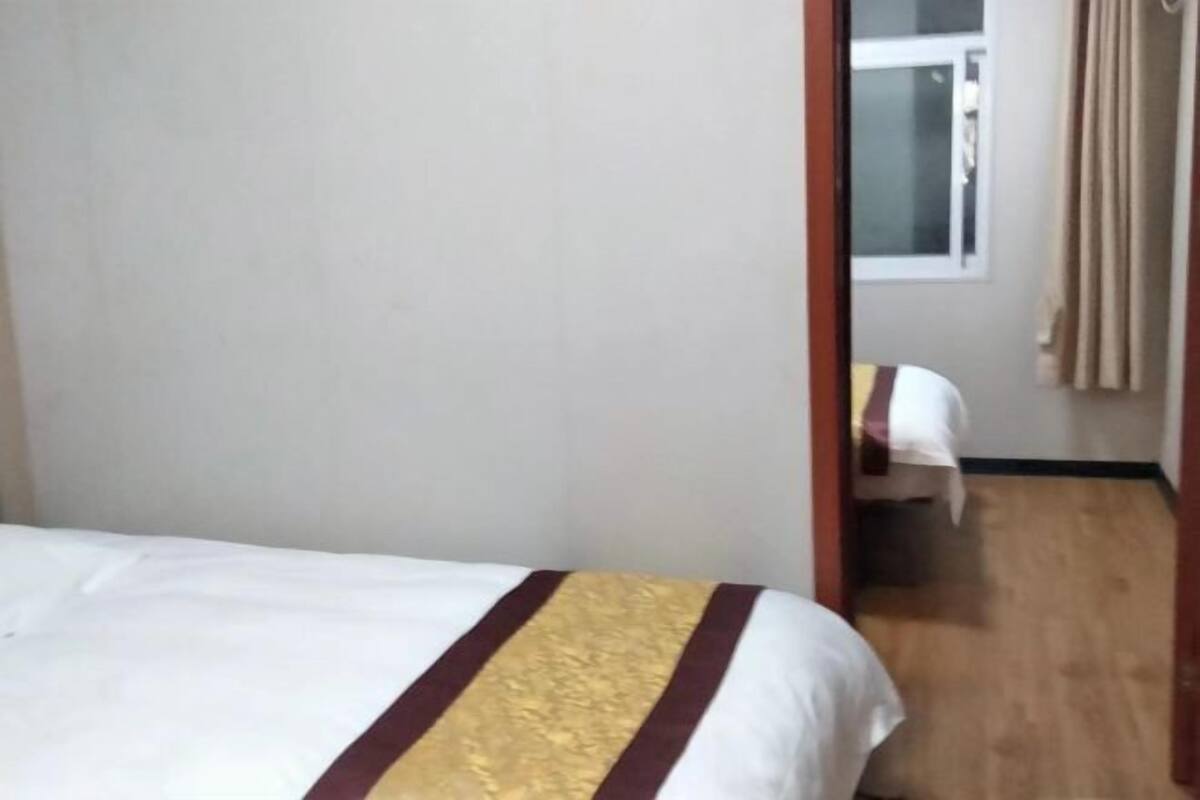 A hotel room with a bed, a window with curtains, and a wooden floor.