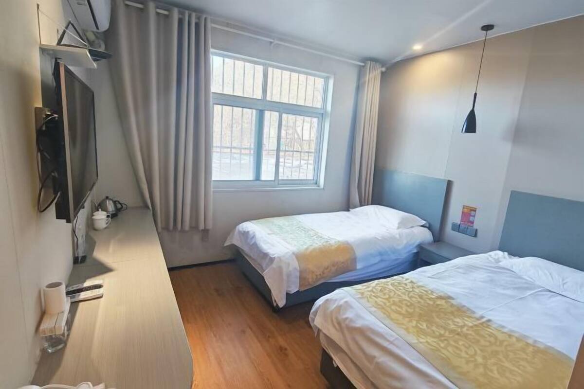 A hotel room with two beds, a TV, a window with curtains, and a ceiling light.