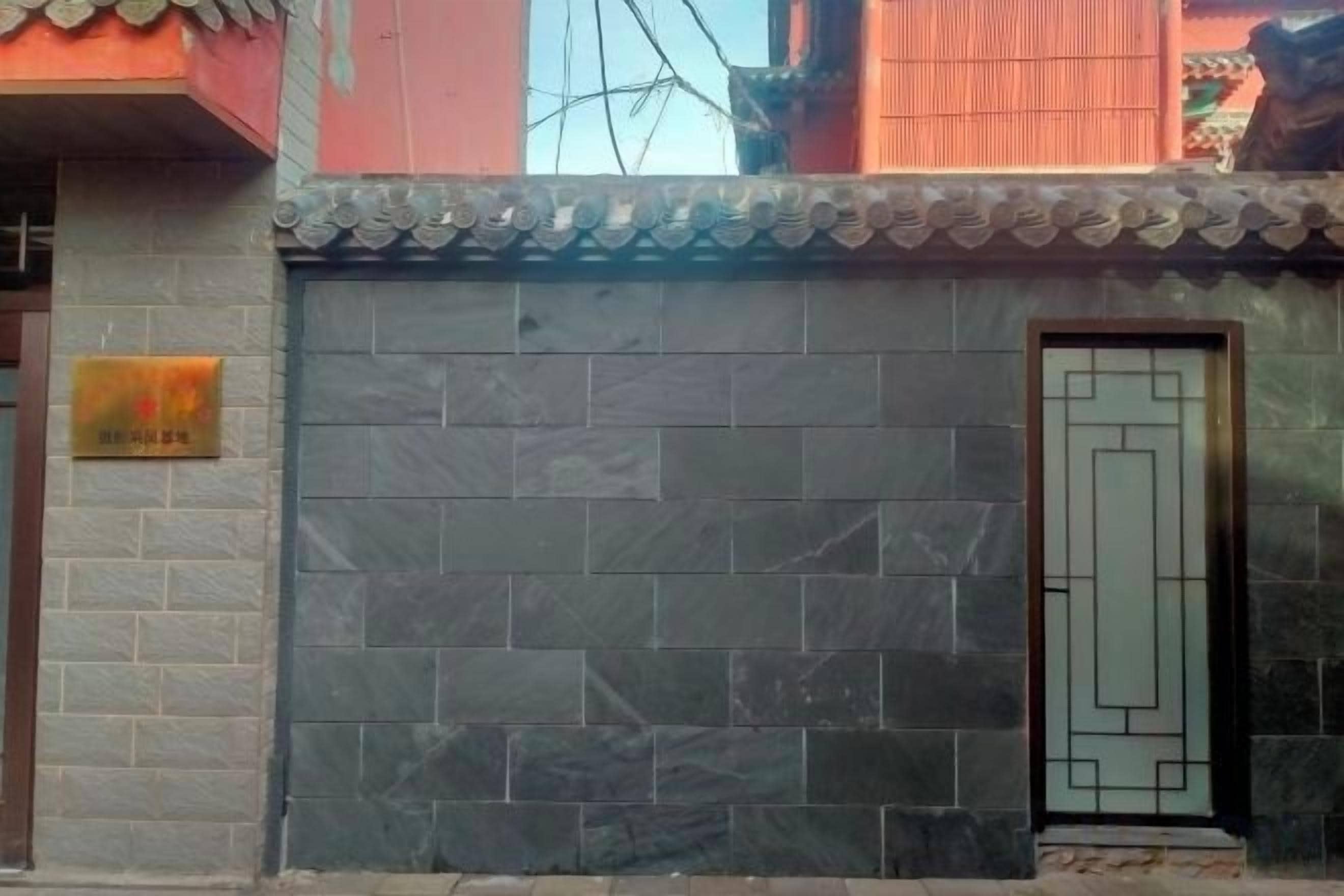 A building facade with a tiled wall, a door with a geometric design, and a sign with Chinese characters.