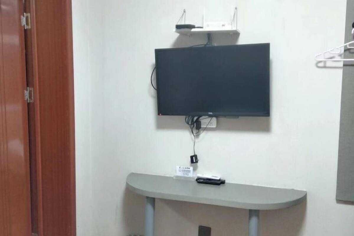 A room with a mounted flat-screen TV, a small table with a remote control, and a door.