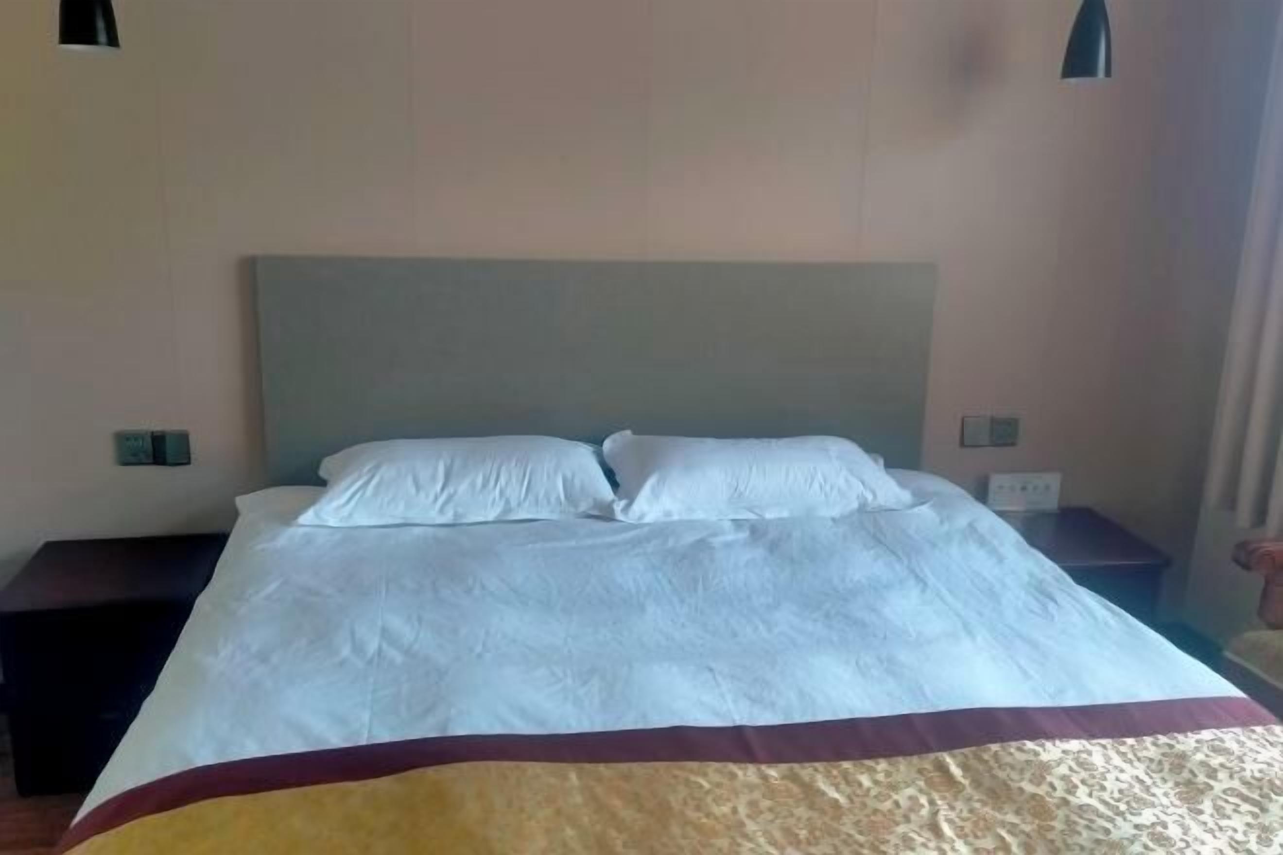 A neatly made bed with white linens and a maroon and beige blanket. There are two bedside tables, one on each side of the bed.