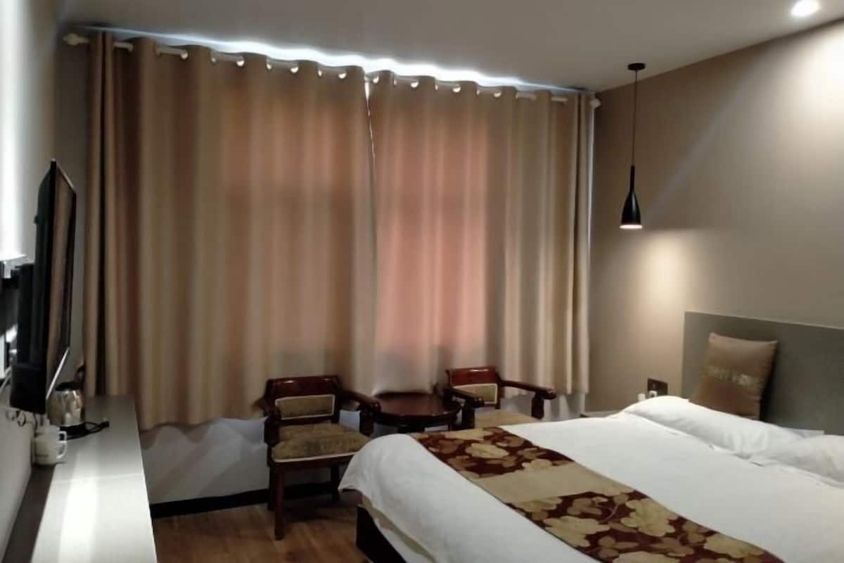 A hotel room with a bed, two chairs, a small table, a TV, and curtains.