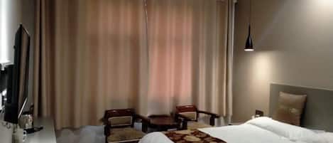 A hotel room with a bed, two chairs, a small table, a TV, and curtains.