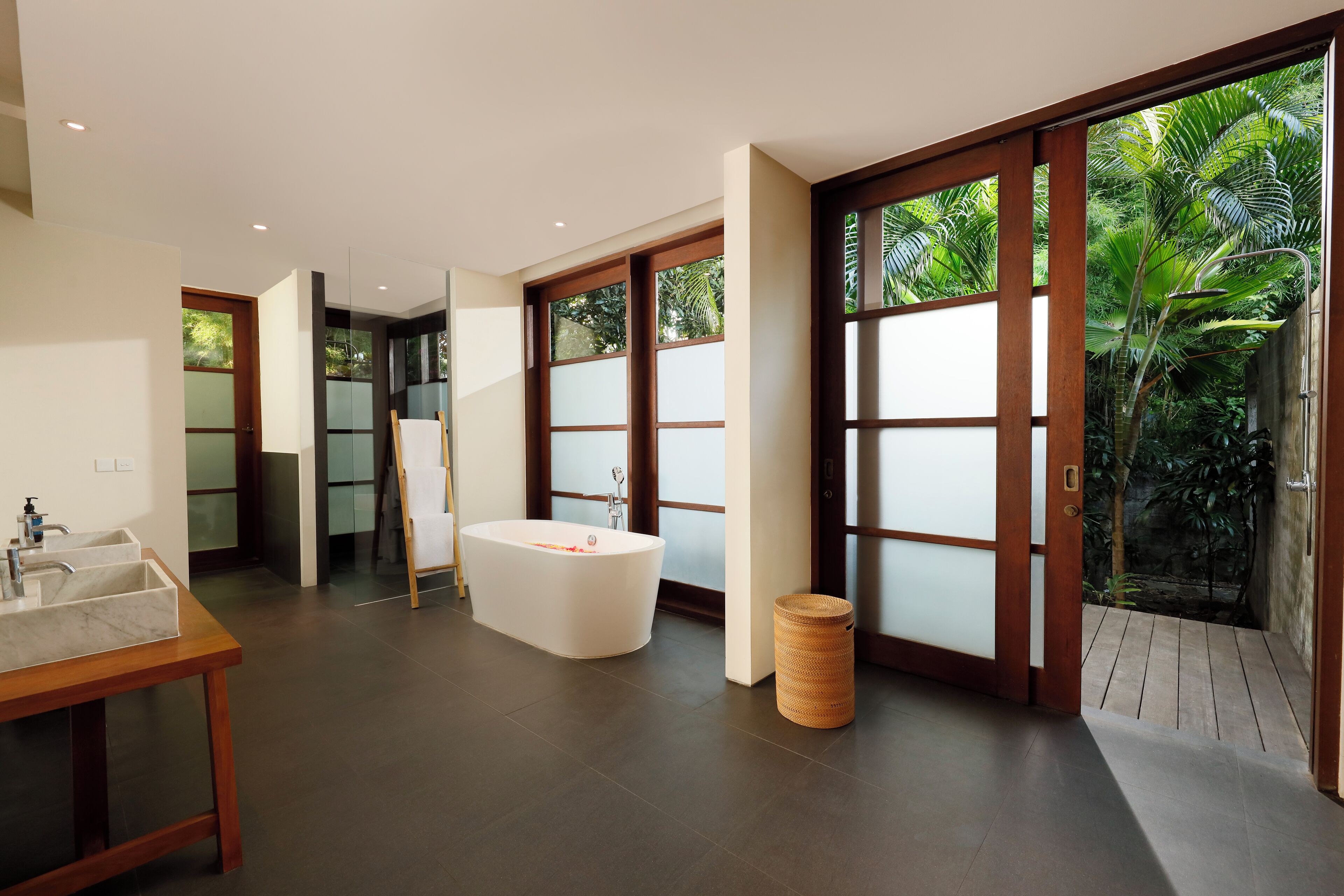 A modern bathroom with a freestanding bathtub, a sink, and a large window with a view of greenery.