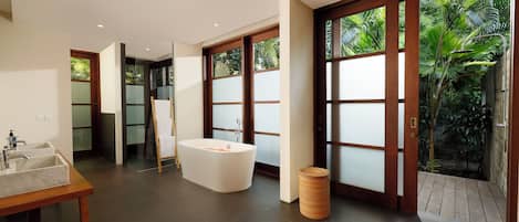A modern bathroom with a freestanding bathtub, a sink, and a large window with a view of greenery.