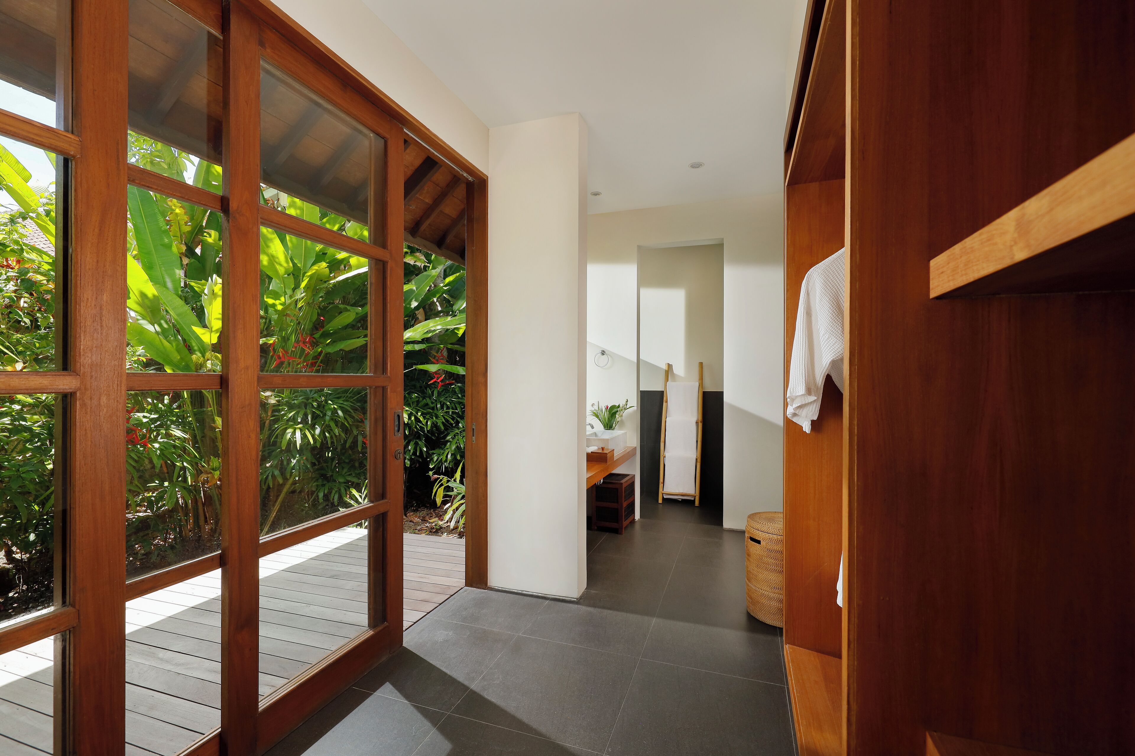 A hallway with a wooden door leading to a balcony with plants.