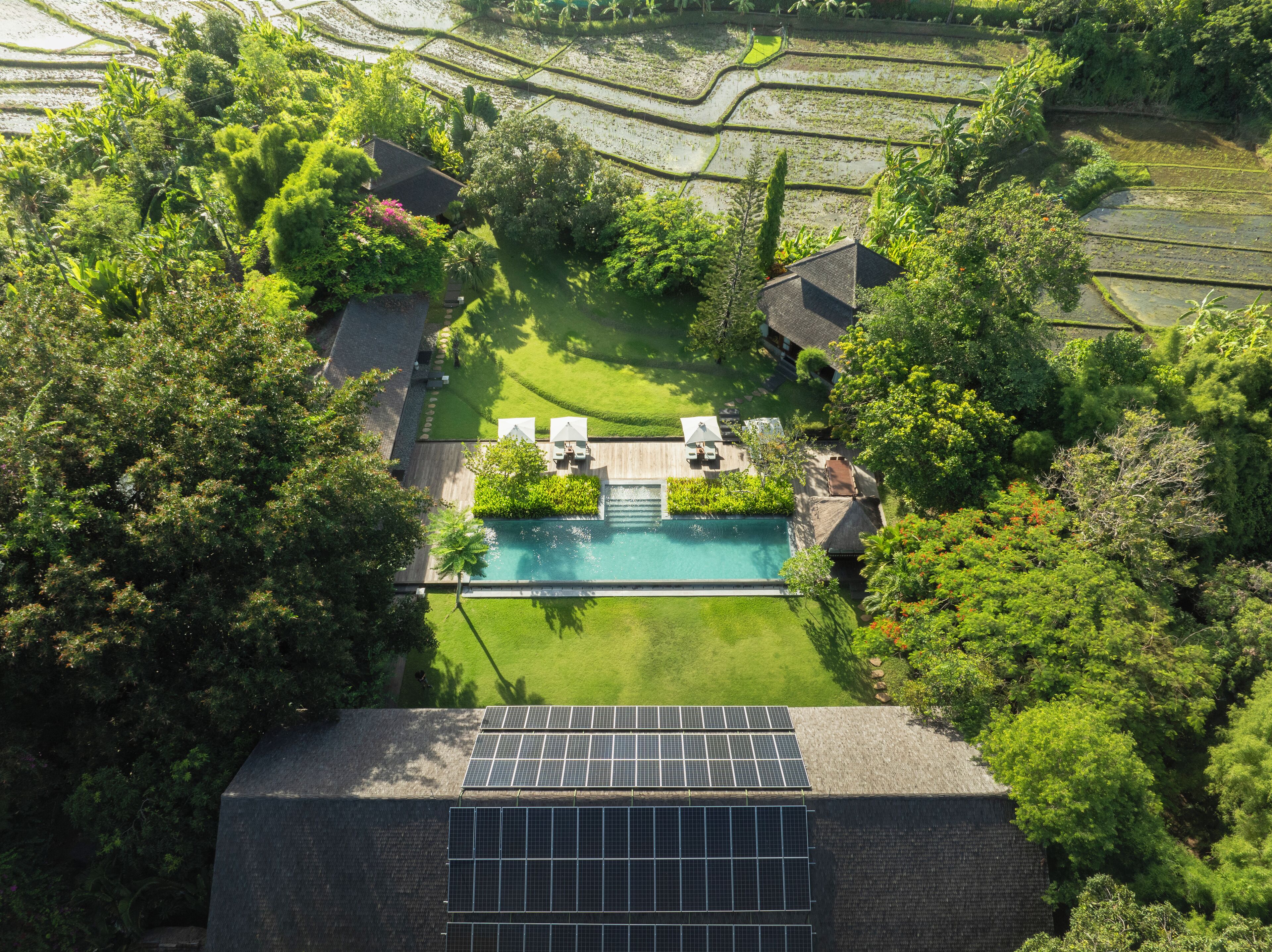 An aerial view of a property with a swimming pool, solar panels, and lush greenery.