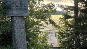 A wooden sign reading "Pinecone Lake Access" with a wooden dock leading to a lake surrounded by trees. - Lakefront Cabin on Back Lake w trail access, and private dock. (Pittsburg)