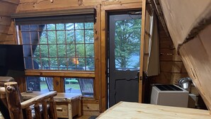 A rustic wooden cabin interior with a dining table, stools, and a kitchen area. - Lakefront Cabin on Back Lake w trail access, and private dock. (Pittsburg)