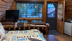 A log cabin bedroom with a bed, a television, a desk, and a window with a view of trees. - Lakefront Cabin on Back Lake w trail access, and private dock. (Pittsburg)