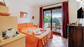 Ein Hotelzimmer mit Bett, Schreibtisch mit Wasserkocher, Tassen und Tablett, Fernseher und Balkon mit roten Vorhängen.