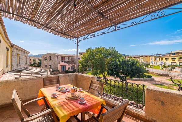 A balcony with a table set for tea, overlooking a courtyard with buildings and trees.
