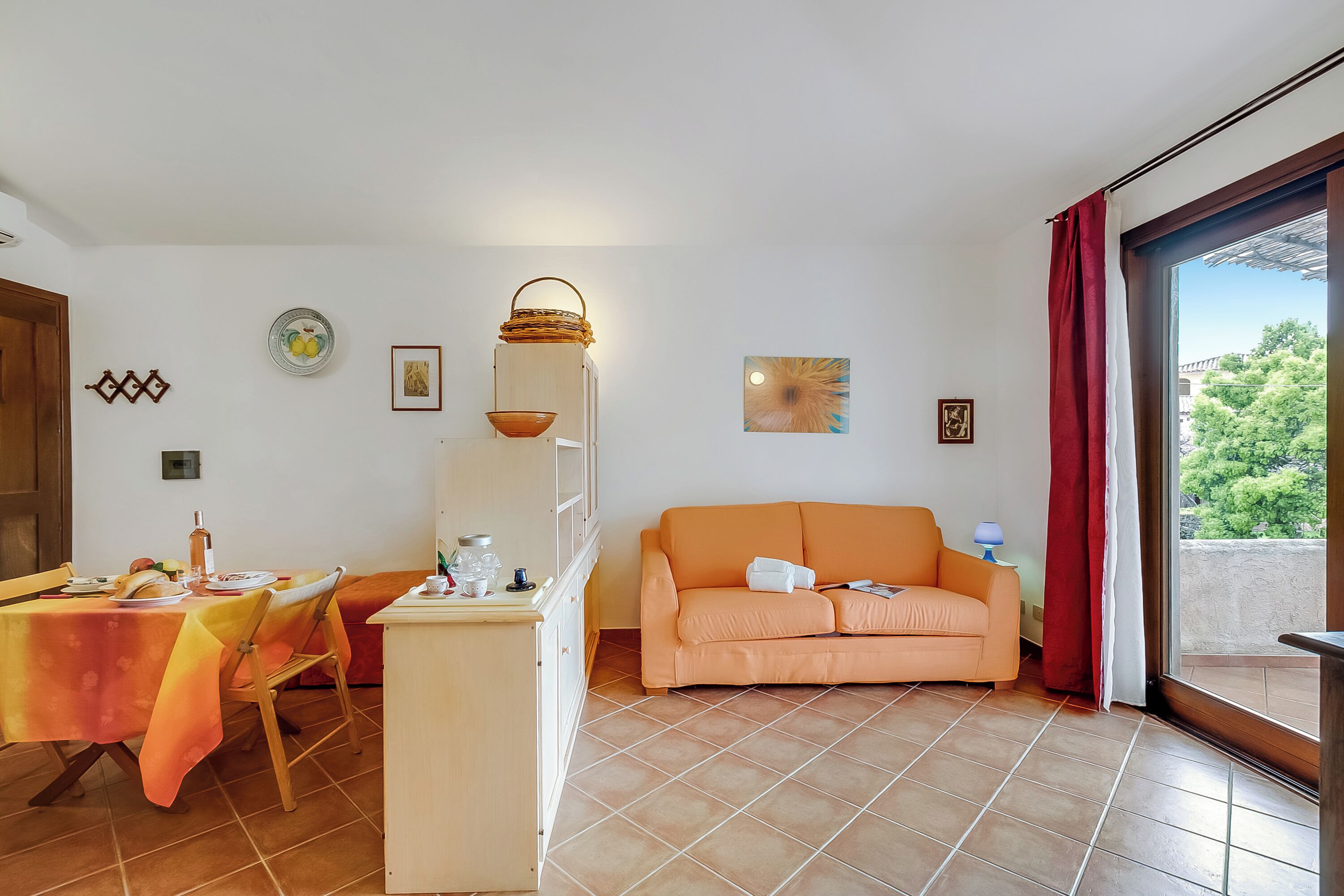 A room with a dining table, a sofa, and a window with curtains.