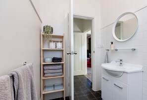 A modern bathroom with a white sink, a round mirror, and a towel rack with folded towels.