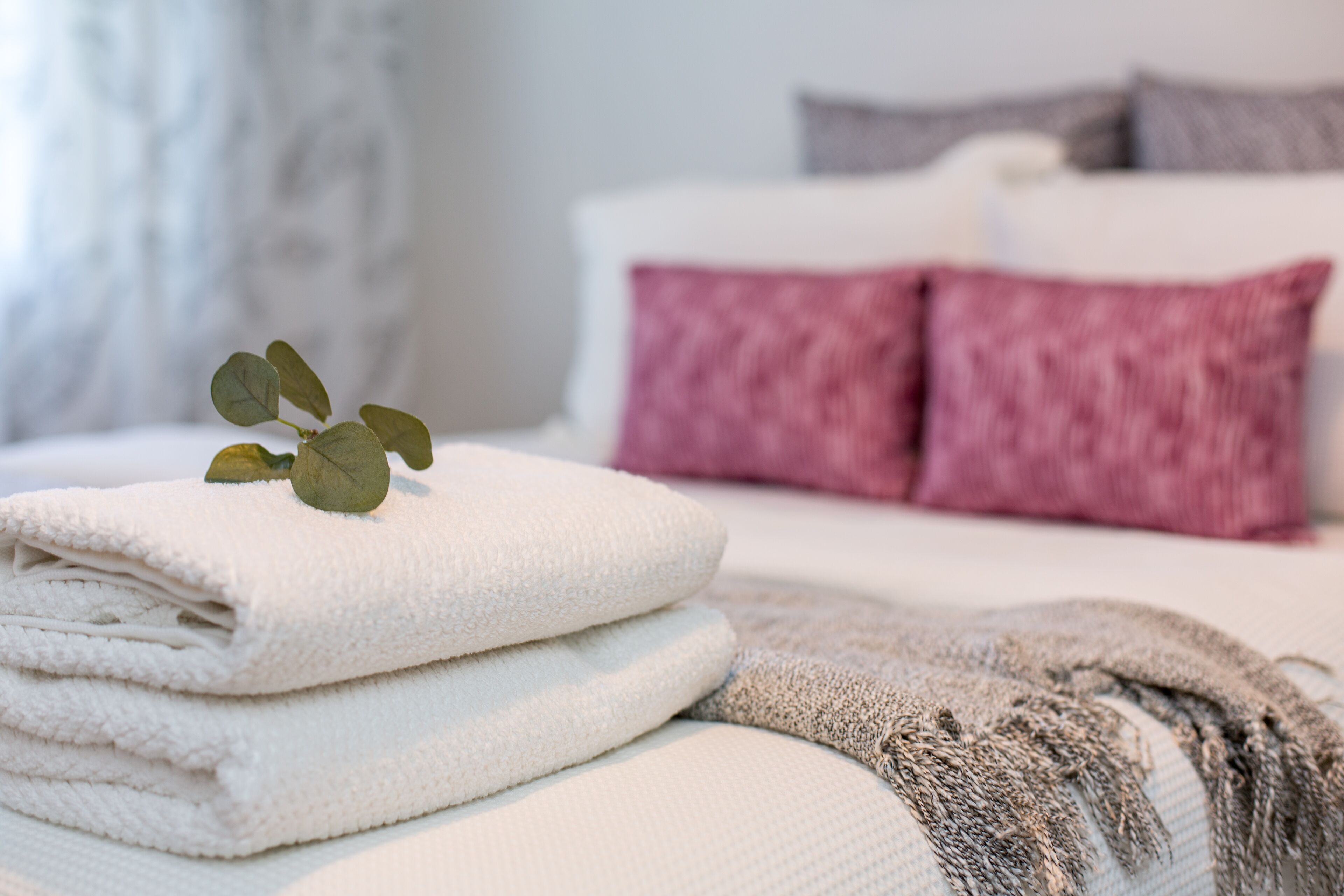 A neatly made bed with white and pink pillows, a folded white towel, and a grey blanket.
