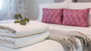 A neatly made bed with white and pink pillows, a folded white towel, and a grey blanket.