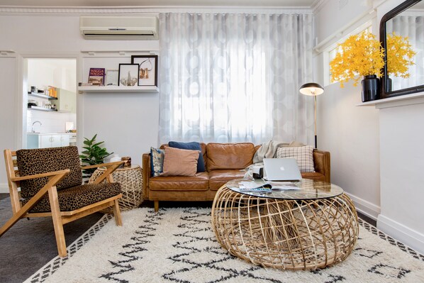 A living room with a brown leather sofa, a leopard print chair, a round wicker coffee table, and a white patterned rug.