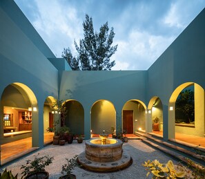 Un patio central con una fuente, rodeado de paseos con arcos y plantas en macetas.
