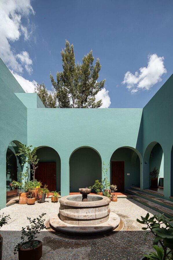 Un patio con una fuente central, plantas en macetas y un árbol grande.