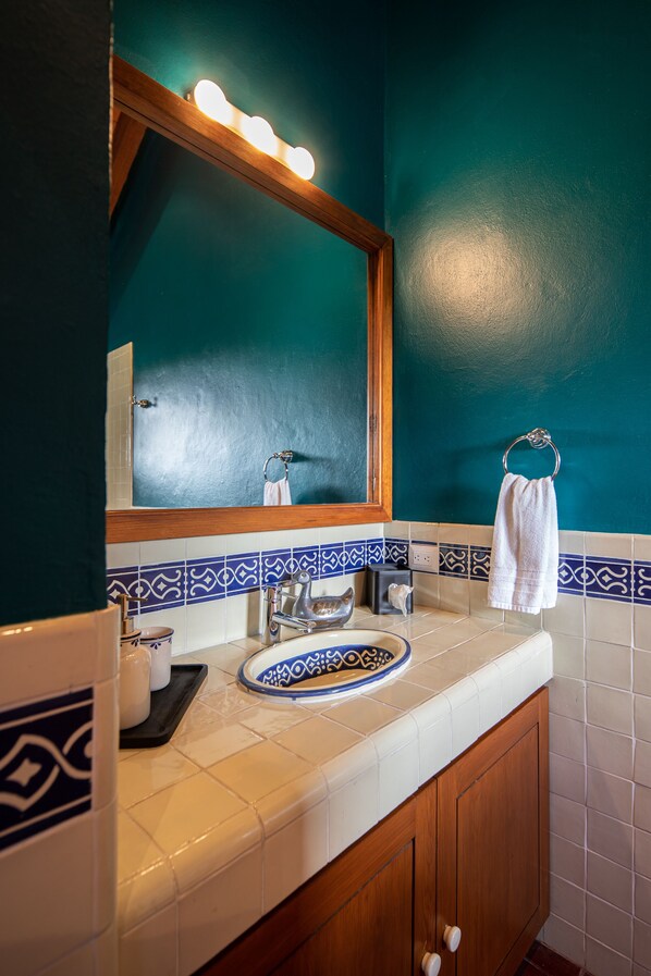 Un baño con pared color turquesa, tocador de madera, espejo con iluminación y un perchero para toallas.