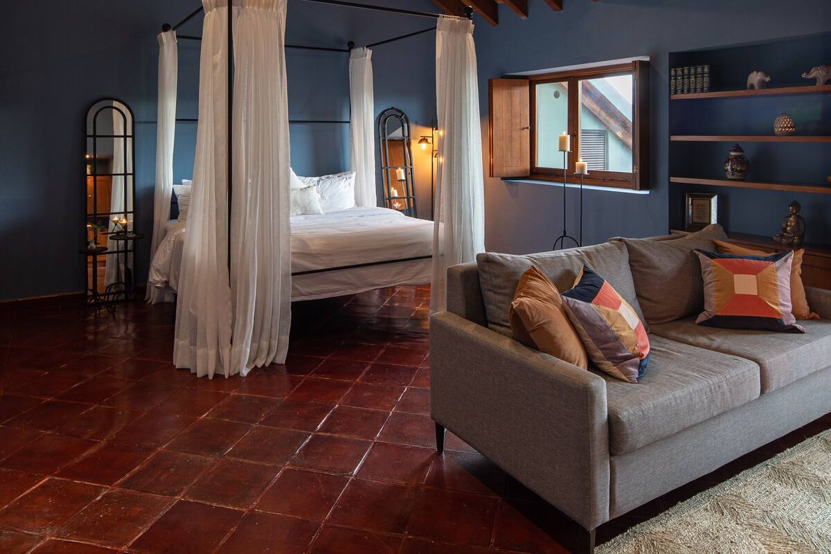 Une chambre à coucher avec un lit à baldaquin, un canapé, un plafond en bois et une table de chevet avec une lampe.