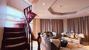 A staircase leading to a landing, a dark-colored sofa with decorative pillows, and a large window with curtains.