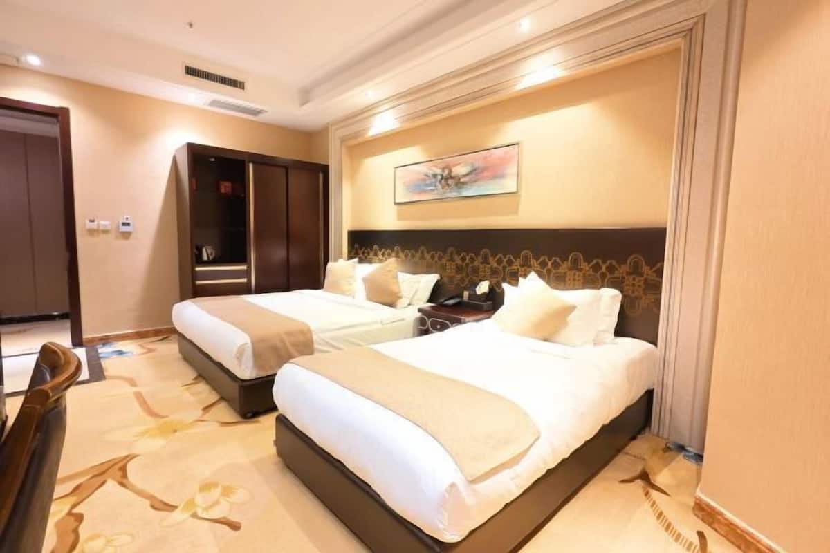 A hotel room with two beds, a wardrobe, a desk, and a painting on the wall.