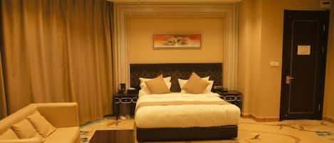 A hotel room with a large bed, a sofa, a coffee table, and a painting on the wall.