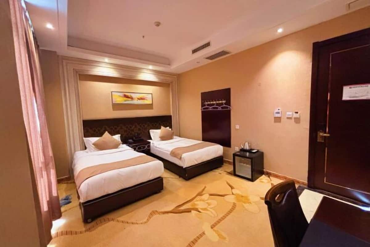 A hotel room with two beds, a desk, a chair, a small table, and a door.