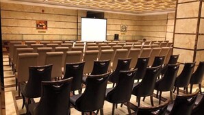 Konferenssihuone, jossa on riveissä tuoleja, projektorikangas ja marmoriseinä.