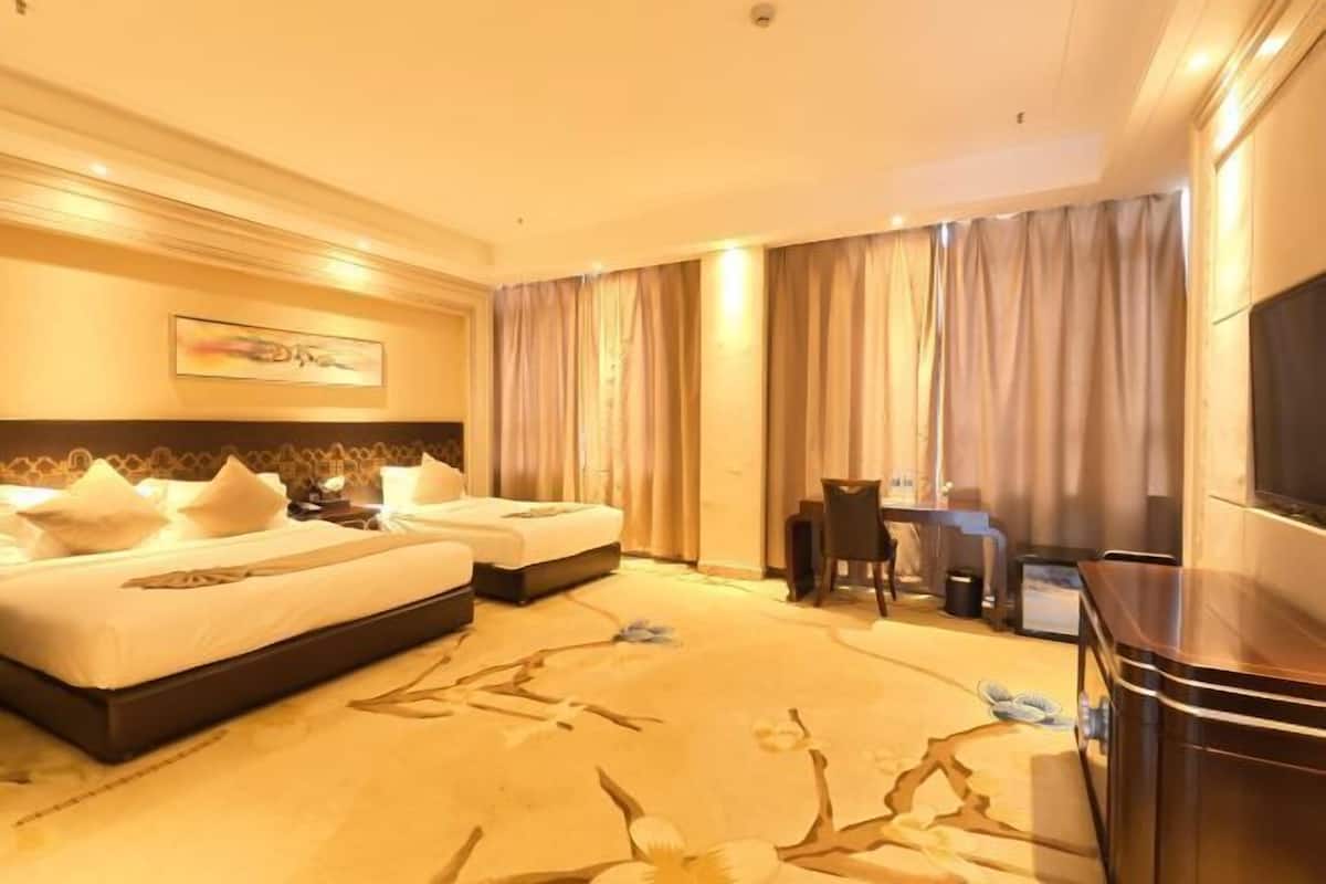 A hotel room with a bed, a desk, a chair, a television, and a large window with curtains.