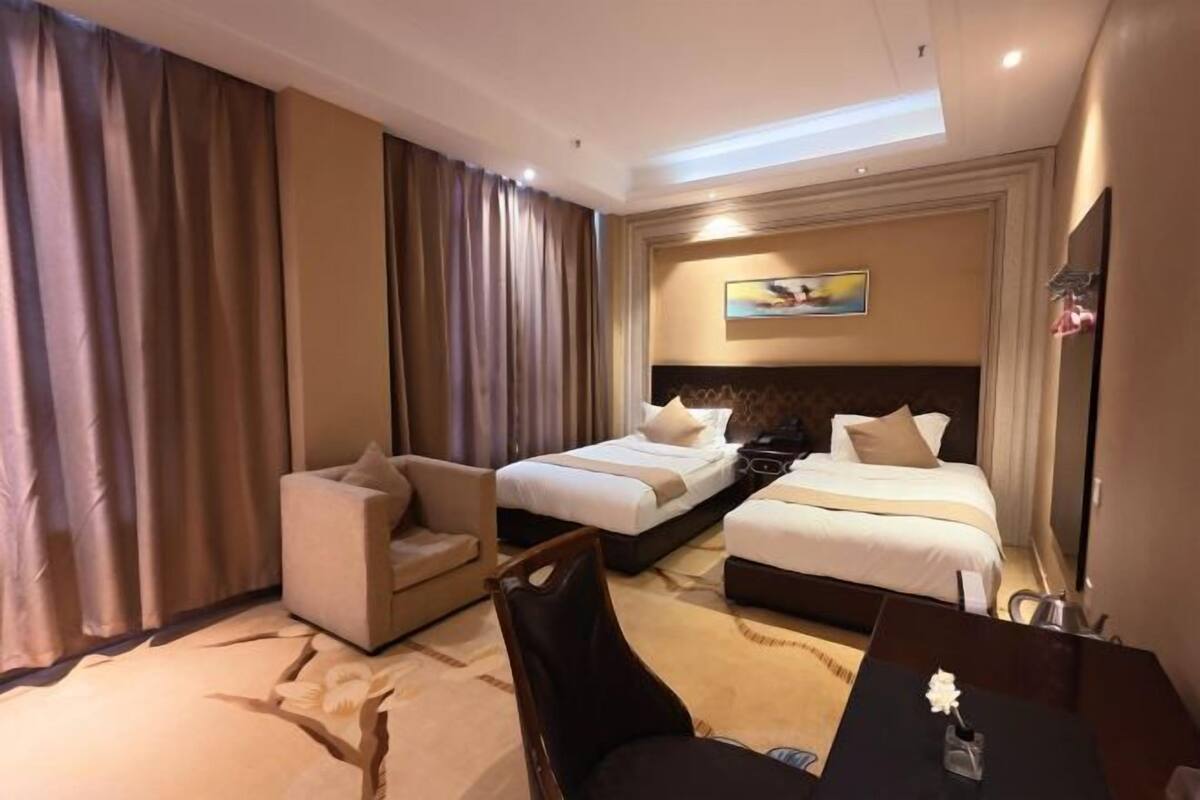 A hotel room with two beds, a sofa, a desk, and a painting on the wall.