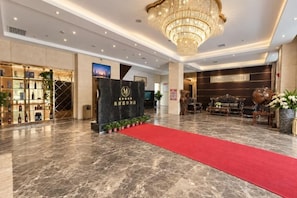 Eine Hotelhalle mit rotem Teppich, einem Empfangstresen und einer Kronleuchter.