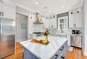 A modern kitchen with white cabinetry, a marble island, stainless steel appliances, and a central island with a floral arrangement. - Stunning Marsh Views, 5 Bedroom 6.5 Bath with pool (Saint Simons Island)
