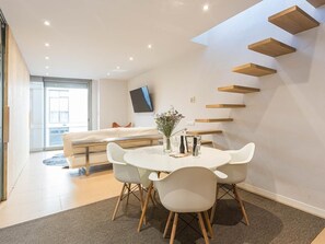 Una sala de estar moderna con comedor, un sofá, un televisor y estanterías empotradas de madera.